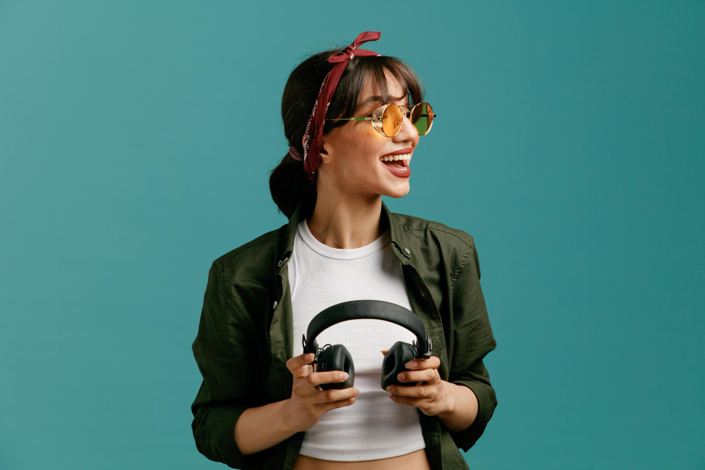 excited-young-student-girl-wearing-bandana-sunglasses-holding-headphones-looking-side-isolated-blue-background cool del bloque